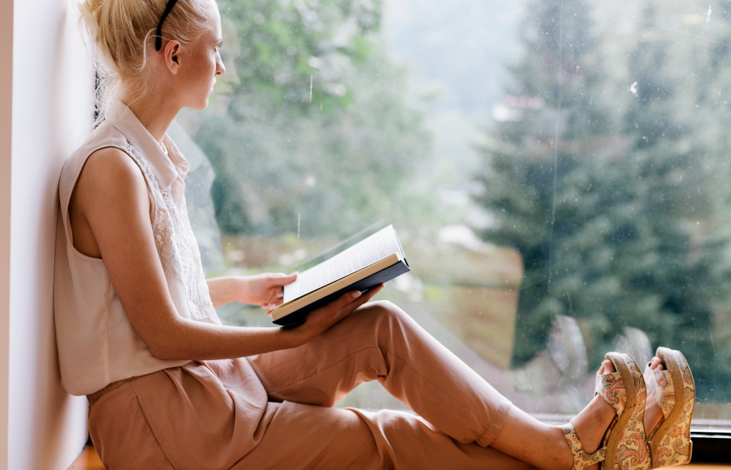 Woman holding a book looking out the window reflectively